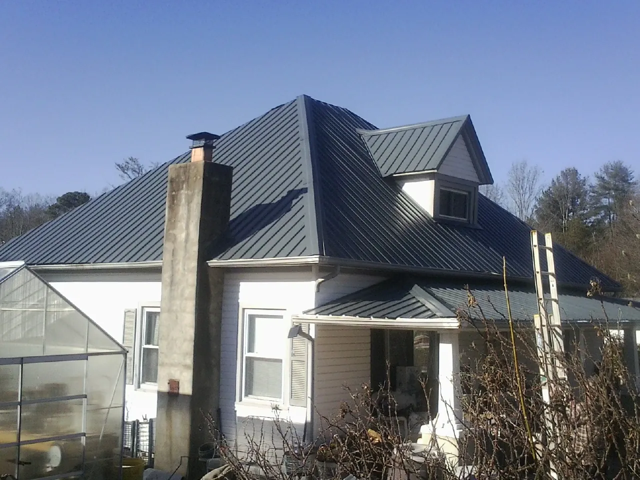 Dark blue standing seam metal roof on a white farmhouse with dormer in Galesville