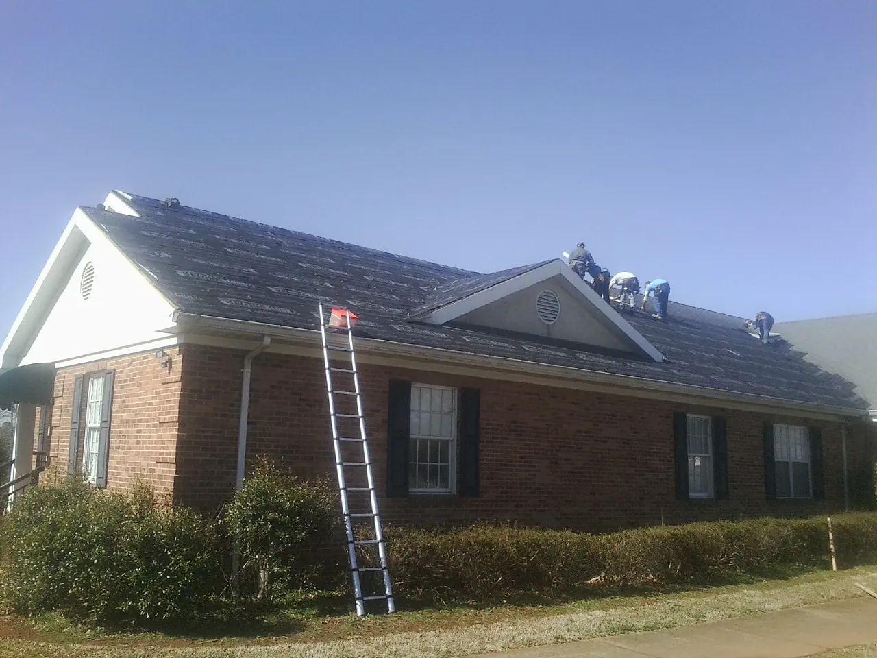 Crew tearing shingles off a brick ranch roof with a ladder set — Metal Roof Repair work by our crew in Galesville