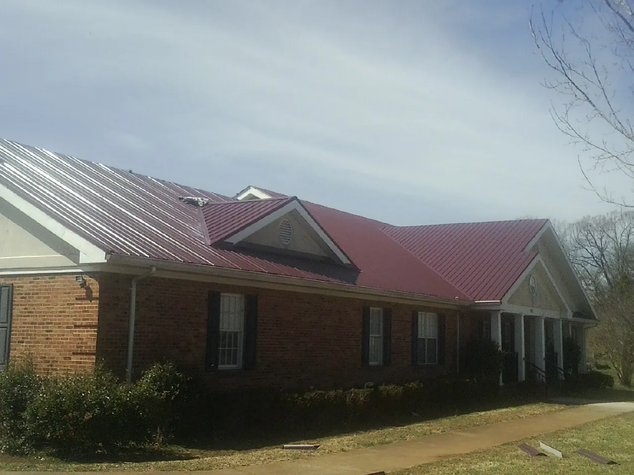 Red metal roof with gabled entries on a long brick building, from a Hail Damage Roof Repair job in Galesville