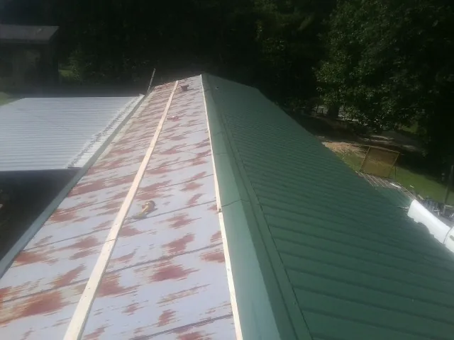 Old rusted panels beside newly installed green metal roofing — Wind Damage Roof Repair by Roofing Brothers in Galesville
