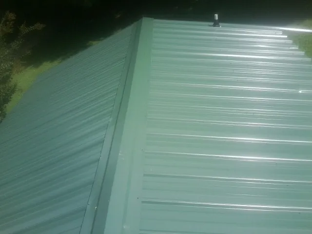 New green metal panels meeting at the ridge of a roof — Flat Roof Repair work by our crew in Galesville