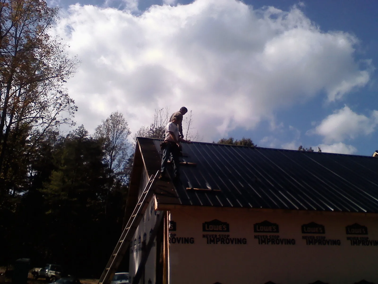 Roofer fastening dark metal panels high against a cloudy sky, from a Roof Inspection job in Galesville
