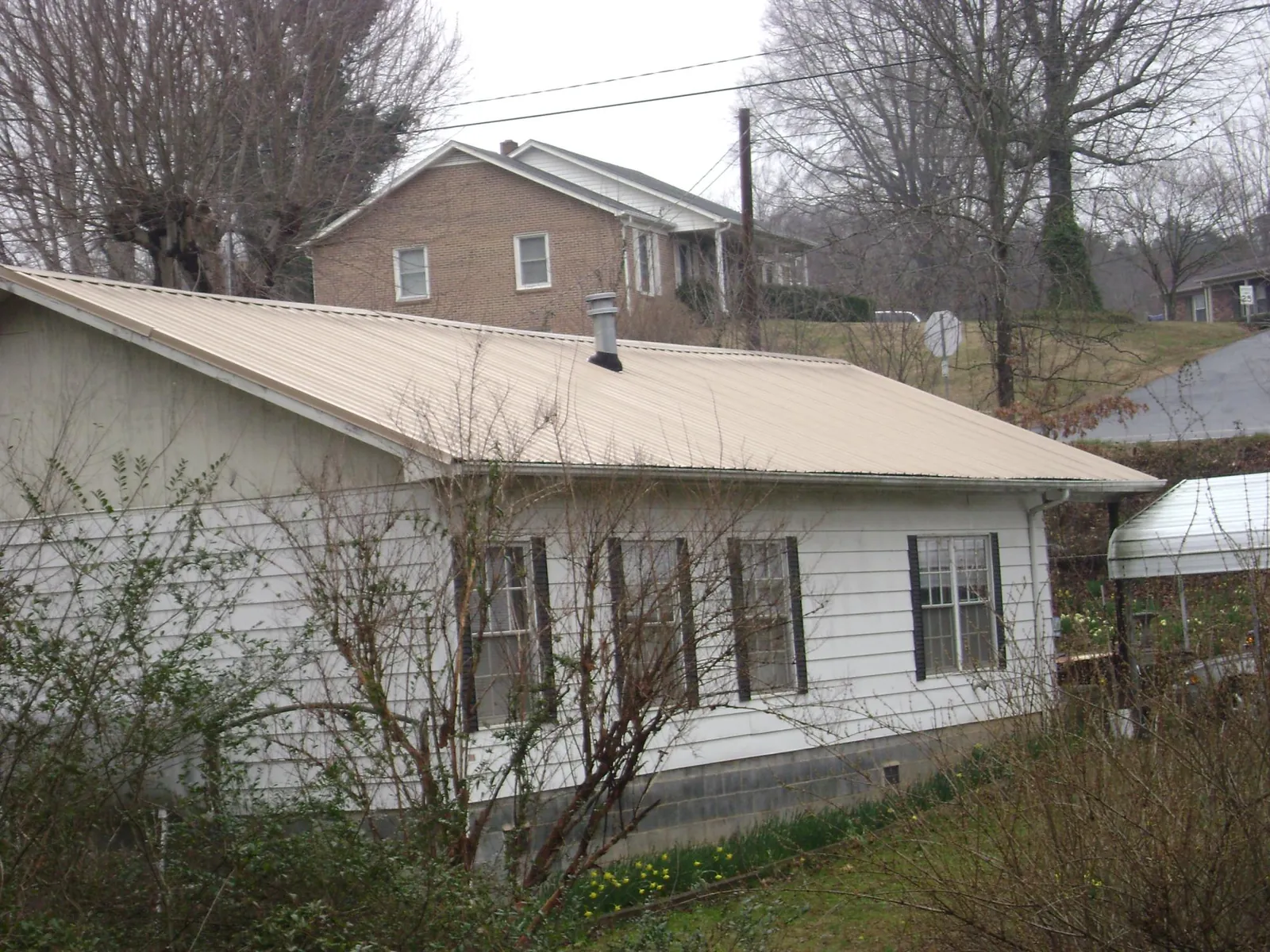 Tan metal roof on a white sided house set into a hillside — Commercial Roofing by Roofing Brothers in Galesville